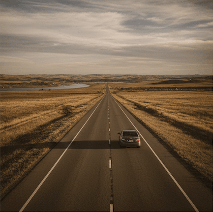 Aerial view of a long straight road cutting through golden-brown South Dakota landscape under cloudy skies